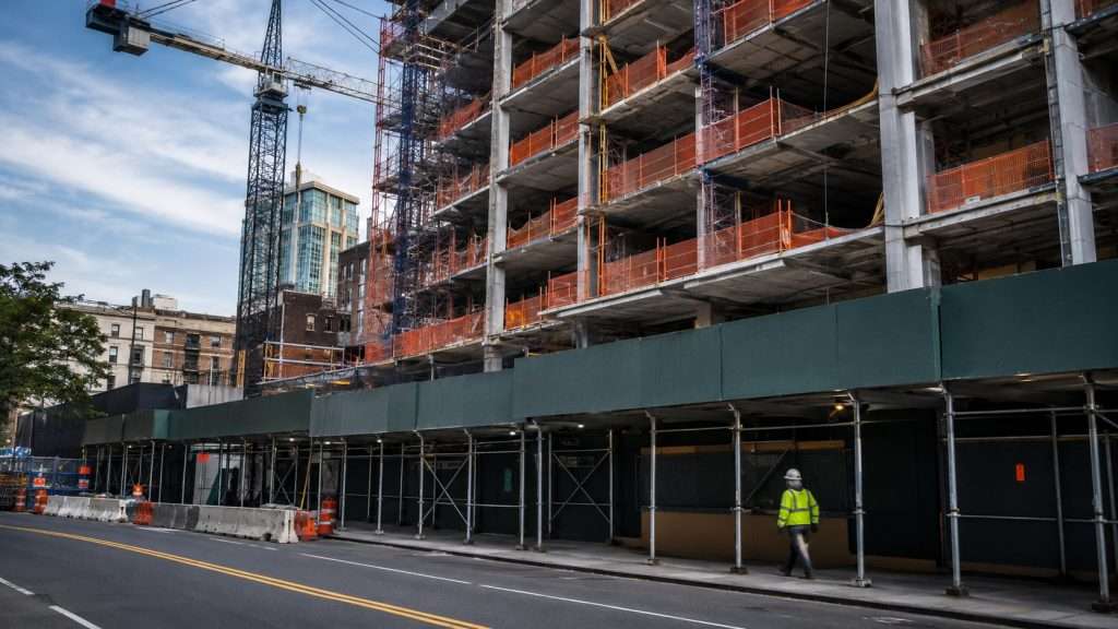 Construction worker walking past scaffolding and a crane at a New York City building site, related to construction accident liability